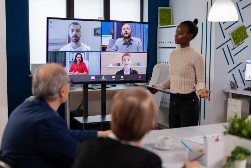 black-manager-woman-talking-with-remotely-colleagues-video-call-tv-screen-presenting-new-business-partners - RumboMag - A virtual workplace is a work environment where employees do not physically come into an office or central location to perform their job duties