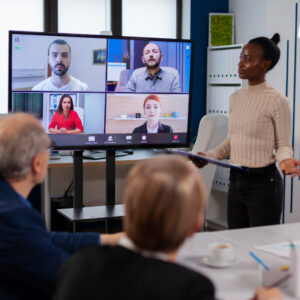 black-manager-woman-talking-with-remotely-colleagues-video-call-tv-screen-presenting-new-business-partners - RumboMag - A virtual workplace is a work environment where employees do not physically come into an office or central location to perform their job duties