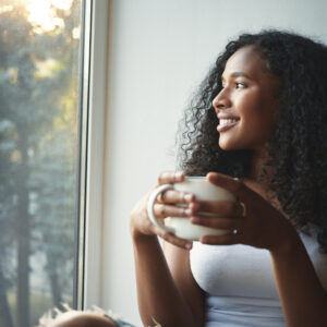morning-routine-portrait-happy-charming-young-mixed-race-female-with-wavy-hair-enjoying-summer-view-through-window-drinking-good-coffee-sitting-windowsill-smiling-beautiful-daydreamer - Positive thinking is looking at things from a positive perspective - RumboMag