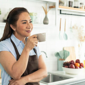 relax-asian-older-woman-apron-holding-cup-coffee-kitchen-room - If you’re a woman over 50, it’s often difficult to know which diet is best, especially as you’re experiencing physical changes associated with aging - Rumbomag