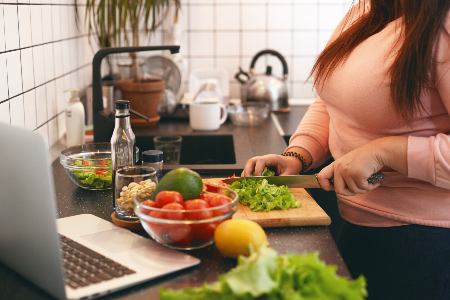 woman-plus-size-female-standing-kitchen-counter-cutting-fresh-organic-vegetables-chopping-board-making-healthy-low-calories-salad-while-watching-movie-online-laptop-computer-RumboMag - Weight loss is a shared goal for some people, and for good reason